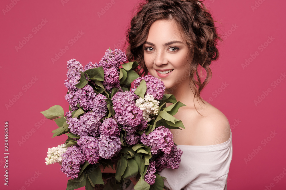 A young slender girl in stylish clothes is holding a bouquet of purple flowers. She is surprised at the gift she was given on a date. On a pink background with space for text A young slender girl in stylish clothes is holding a bouquet of purple flowers. She is surprised at the gift she was given on a date. On a pink background with space for text