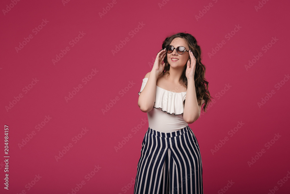 A young girl in sunglasses dreams of traveling, flying on an airplane and summer vacation on the beach. Standing on a pink isolated background with space for text A young girl in sunglasses dreams of traveling, flying on an airplane and summer vacation on the beach. Standing on a pink isolated background with space for text