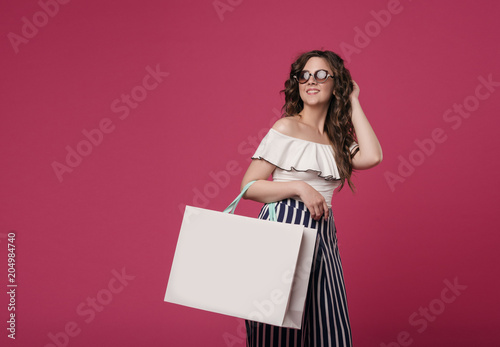 A young slender girl in stylish clothes is holding a large white bag. She hurries to the store for a sale. On a pink background with space for text