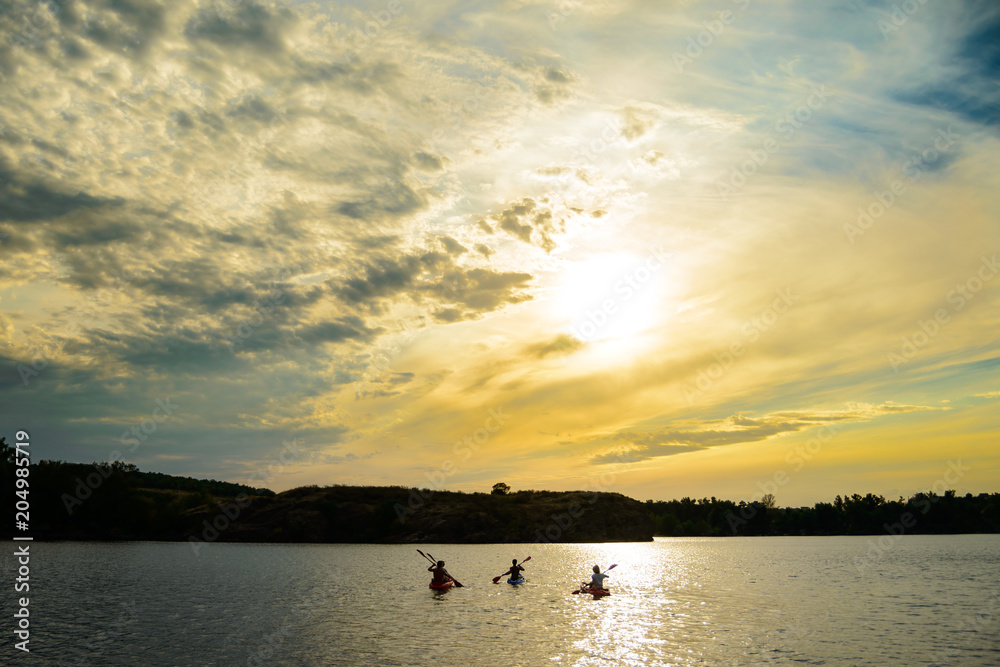 Friends Paddling Kayaks on the Beautiful River or Lake under Dramatic Evening Sky at Sunset