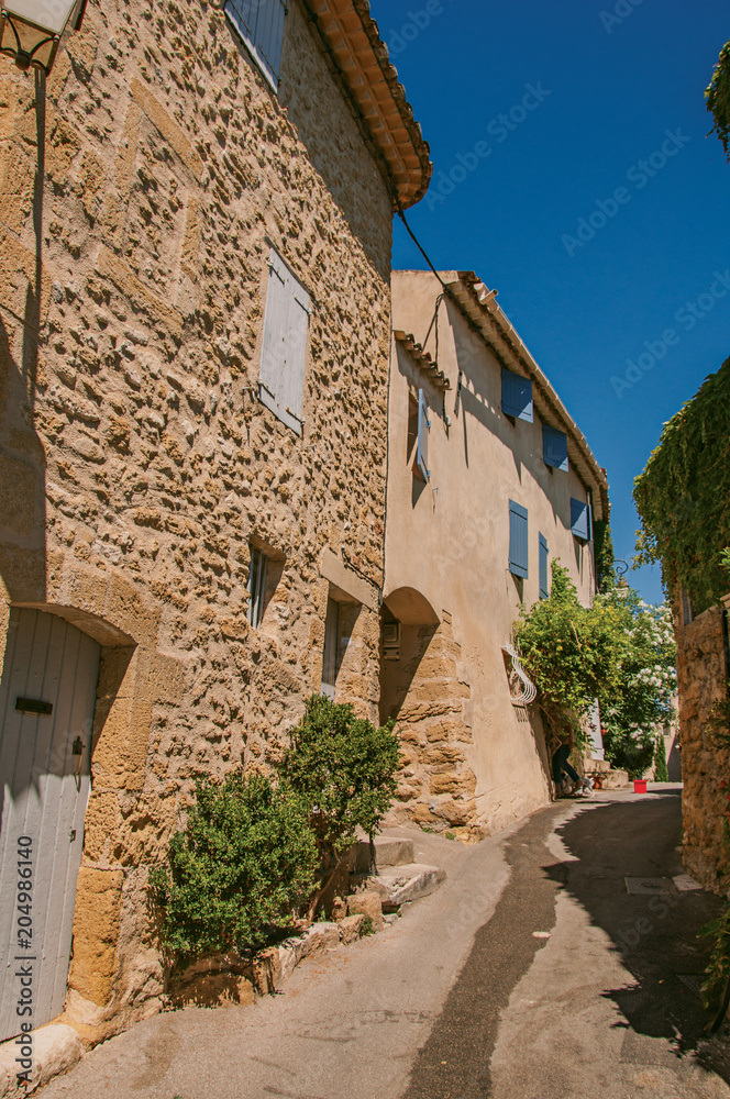 View of typical stone houses with sunny blue sky, in a raised alley of the historical village of Lourmarin. In the Vaucluse department, Provence-Alpes-Côte d'Azur region, southeastern France