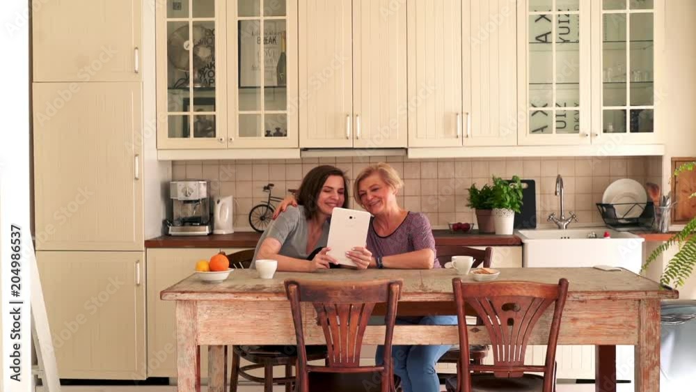 Mother with daughter chatting on tablet sitting in the kitchen
Mother with daughter chatting on tablet sitting in the kitchen