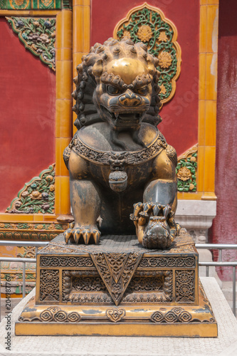 Beijing, China - April 27, 2010: Forbidden City. Closeup of brown-yellow lion in front of red wall with green and yellow decorations.