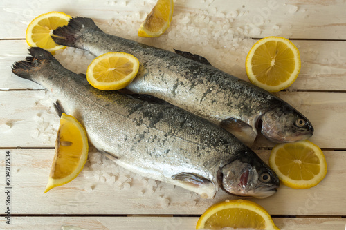 Rainbow trout over sea salt with pieces of lemon over white Mediterranean wooden background