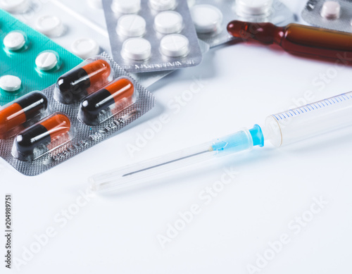 Syringe and pills in blisters on a white table. Copy space