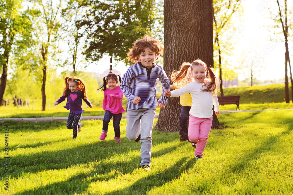 many young children smiling running along the grass in the park. Childhood, Children's Day, vacation, vacation, adventure, friendship. - obrazy, fototapety, plakaty 