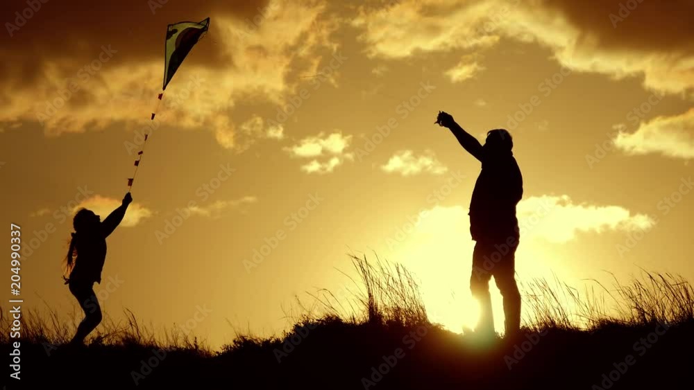 Silhouette of a happy family playing a kite. Grandpa and little girl are playing at sunset with a kite. Silhouette of a happy family playing a kite. Grandpa and little girl are playing at sunset with a kite.