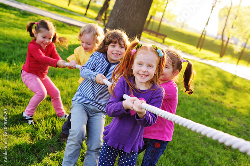 a group of small preschool children play a tug of war in the park. Outdoor games, childhood, friendship, leadership, children's day.