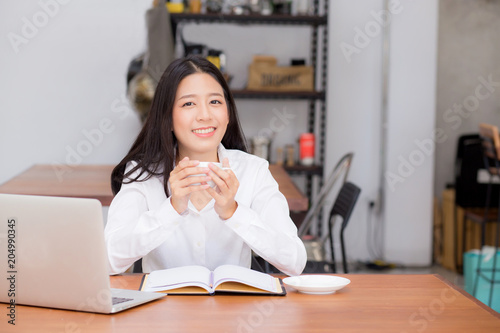Beautiful asian young woman working online on laptop and drink coffee sitting at coffee shop, professional female freelancer using notebook computer with connect to internet for distance job.