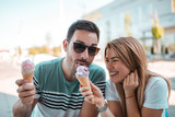 Young couple sharing ice cream while enjoying sunny weather outdoors