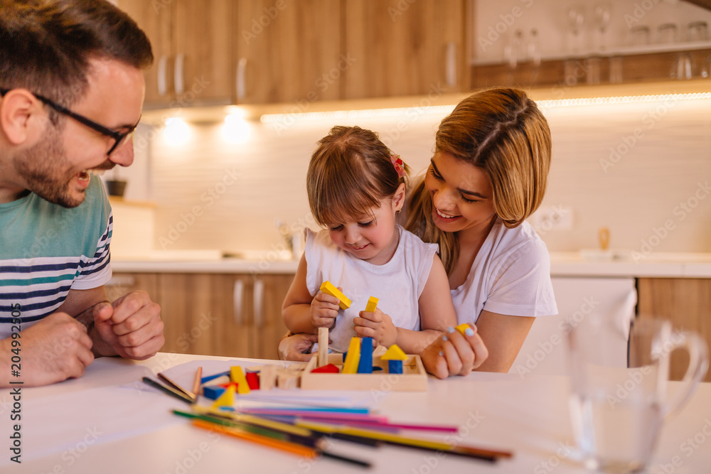 Young happy family of three playing with wooden toys on kitchen table at home Young happy family of three playing with wooden toys on kitchen table at home