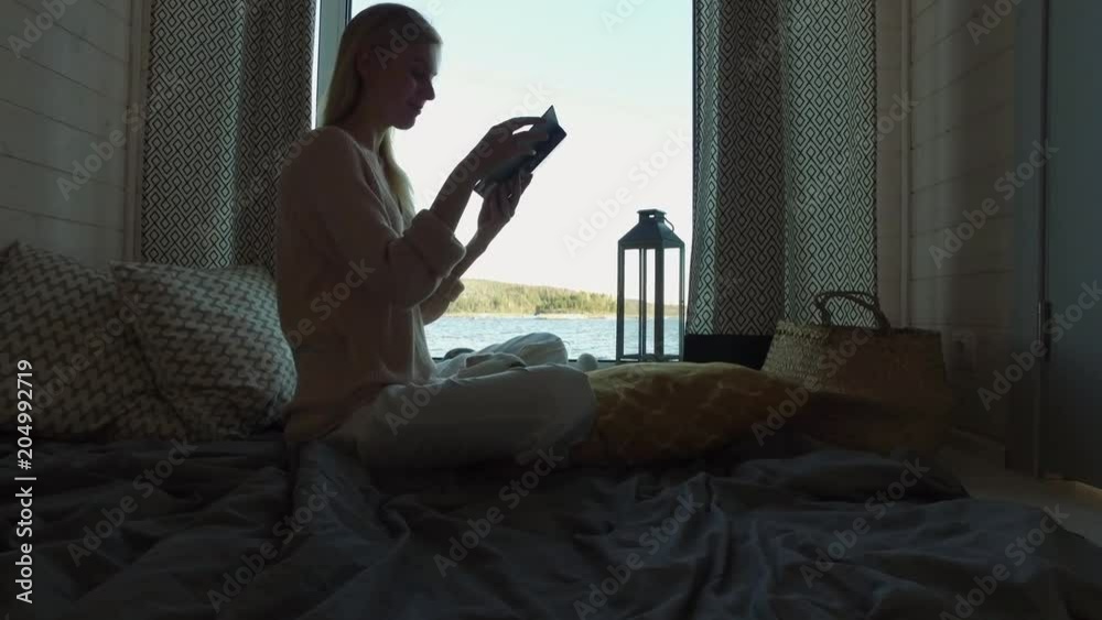 young woman reading a book by the window with a lake view young woman reading a book by the window with a lake view