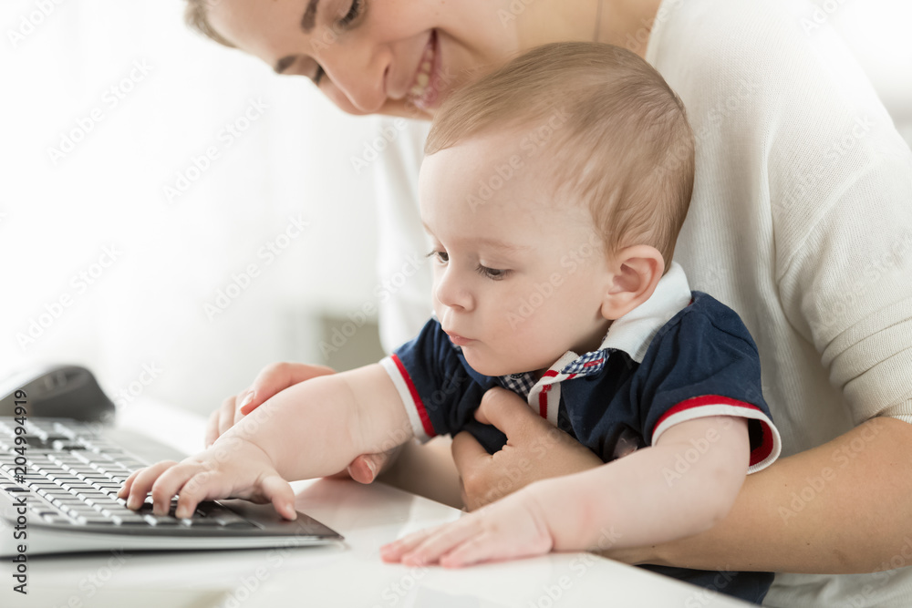 Cute baby boy sitting on mothers lap in office and typing on computer keyboard Cute baby boy sitting on mothers lap in office and typing on computer keyboard