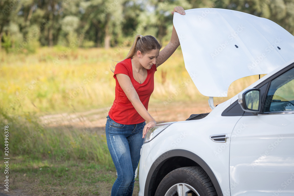 Young depressed woman looking on the engine of broken car in field Young depressed woman looking on the engine of broken car in field