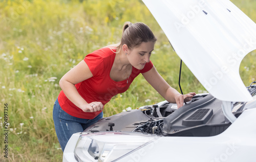 Portrait of young woman fixing her broken car in field