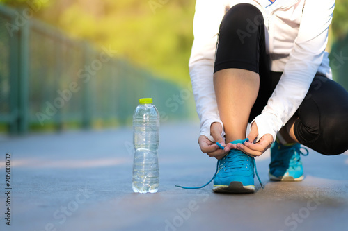 young fitness woman legs walking in the park outdoor, female runner tying running shoes, asian girl jogging and exercise on footpath in sunlight morning. healthcare and well being concepts