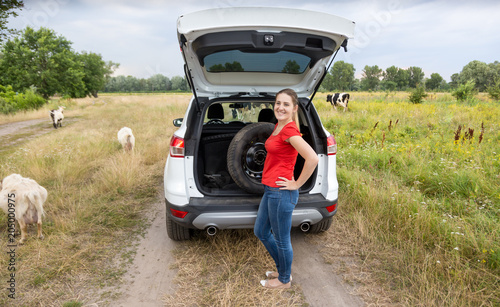 Young smiling woman standing at broken car on countryside road next to farm © Кирилл Рыжов