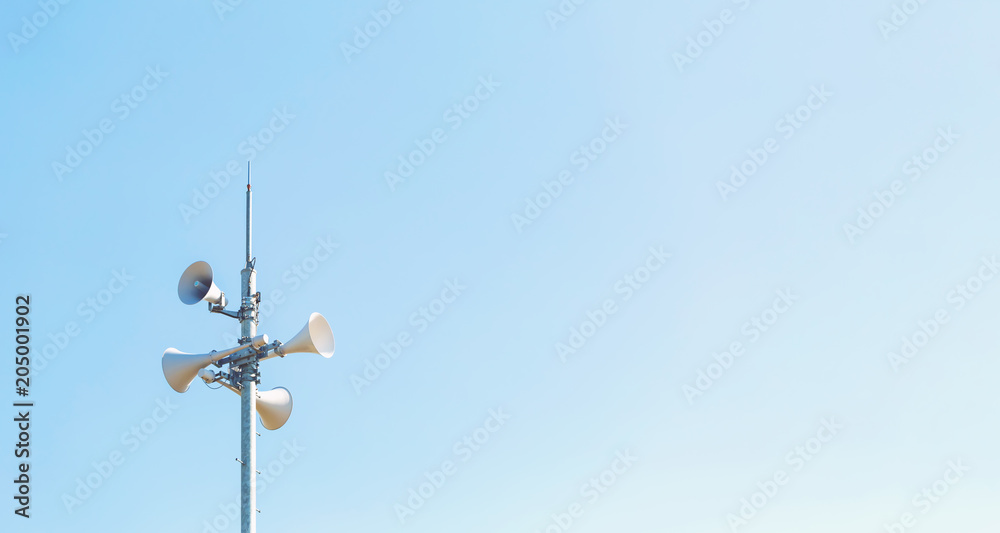Outdoor loudspeaker alert system against a blue sky