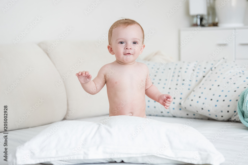 Portrait of adorable 9 months old baby boy sitting on bed with white bed linen Portrait of adorable 9 months old baby boy sitting on bed with white bed linen