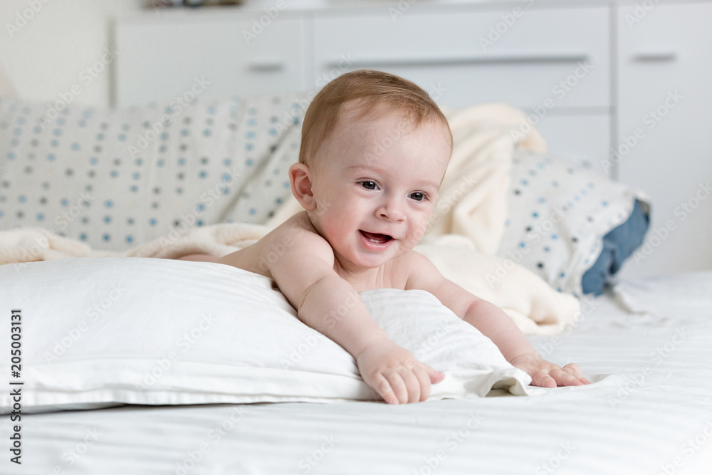 Portrait of adorable 9 months old baby boy lying on big pillow on bed