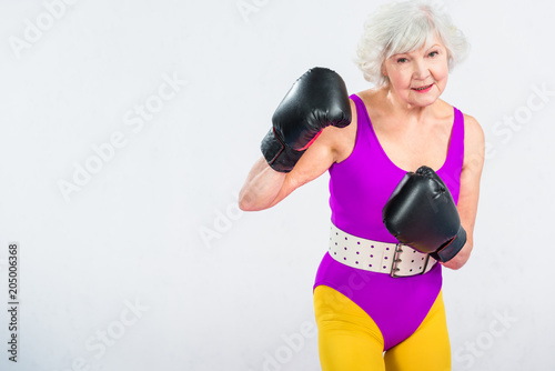 sportive senior lady boxing and smiling at camera isolated on grey