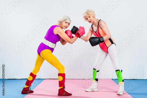 full length view of senior sportswomen in boxing gloves training and looking at camera