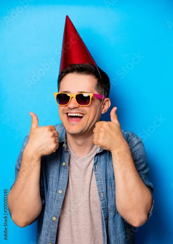 Canvas Print Young man in birthday hat and sunglasses on blue background