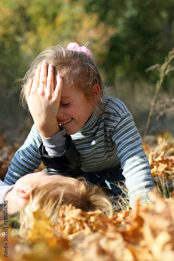Naklejka premium A woman with a smiling little girl are playing on the ground covered by yellow foliage