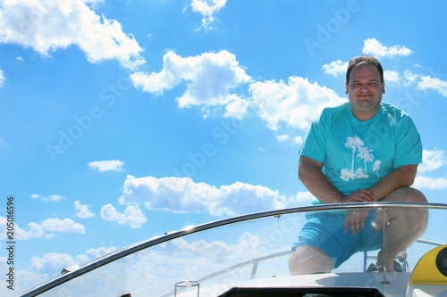 smiling man in blue clothes in a boat on a background of smooth water of a blue cloudy sky