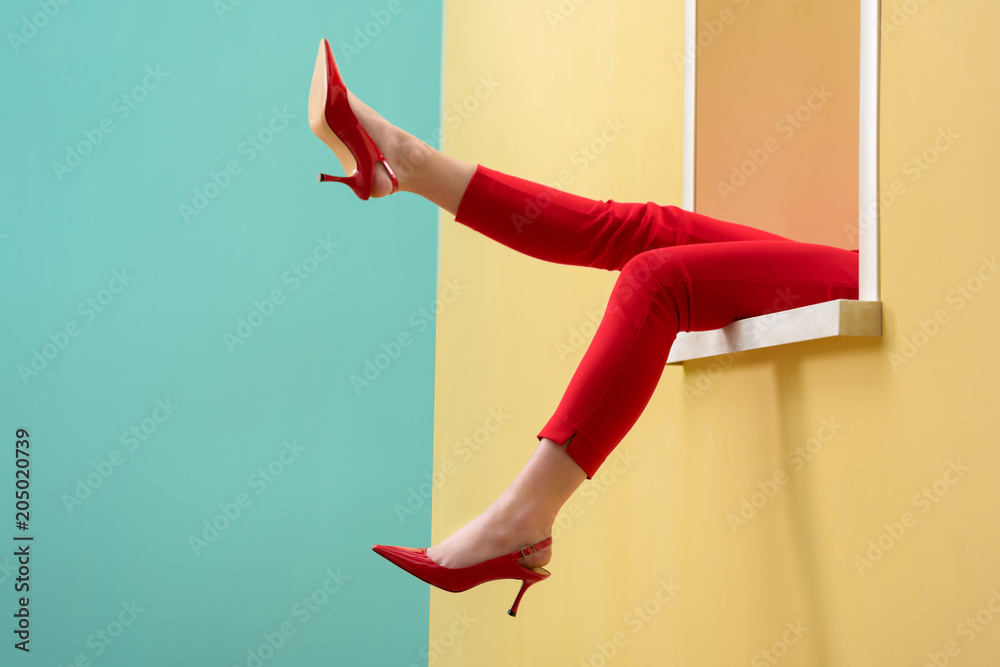 partial view of woman in red pants and shoes outstretching legs out decorative window - obrazy, fototapety, plakaty 