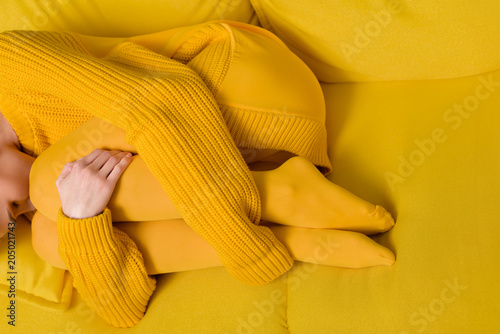 partial view of woman in yellow sweater and tights sleeping on yellow sofa