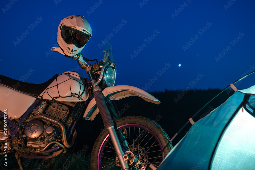 Night camping in the mountains forest. tourist have a rest at a campfire near illuminated tent under amazing night sky. Low light. off road motorcycle adventure, enduro.
