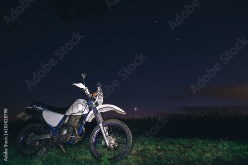 Night camping in the mountains forest. tourist have a rest at a campfire near illuminated tent under amazing night sky full of the star. Low light. off road motorcycle adventure, enduro.
