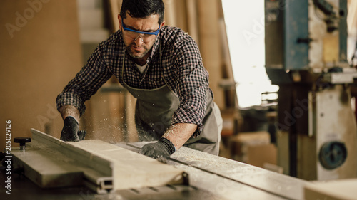 Skilled carpenter cutting a piece of wood in his woodwork workshop