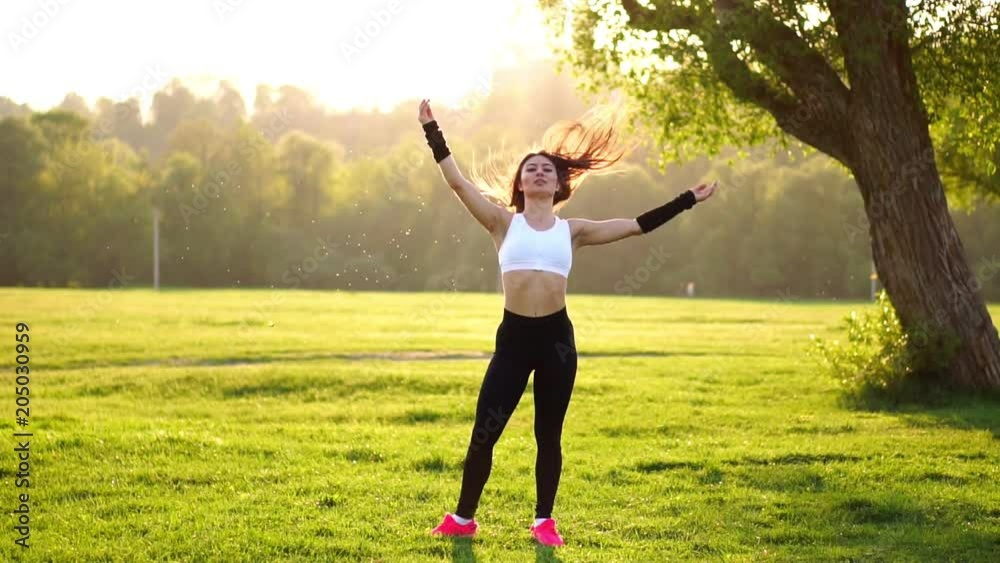 Young and beautiful woman is sitting on the mat during break in her fitness workout. Rest after exercise in the sunlight correcting the hair in slow motion. Hair in the backlight. Young and beautiful woman is sitting on the mat during break in her fitness workout. Rest after exercise in the sunlight correcting the hair in slow motion. Hair in the backlight.