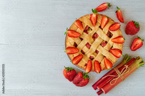 Homemade rhubarb strawberry pie on the gray kitchen background with copy space. Vegetarian summer pie decorated with fresh organic ingredients - sliced strawberries and raw rhubarb. Top view