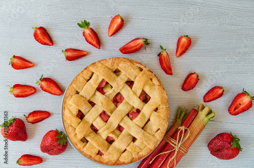 Traditional rhubarb strawberry pie on the gray kitchen table. Vegetarian pie decorated with fresh organic ingredients - sliced strawberries and raw rhubarb. Delicious healthy summer dessert. Top view
