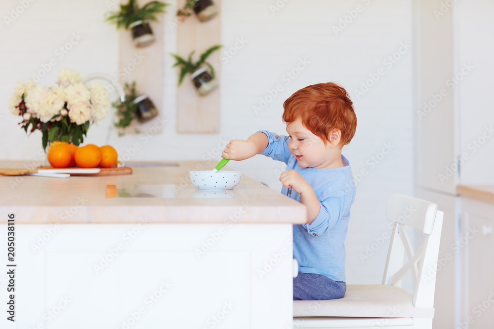 cute happy toddler baby boy sitting at the table, having breakfast in the morning cute happy toddler baby boy sitting at the table, having breakfast in the morning