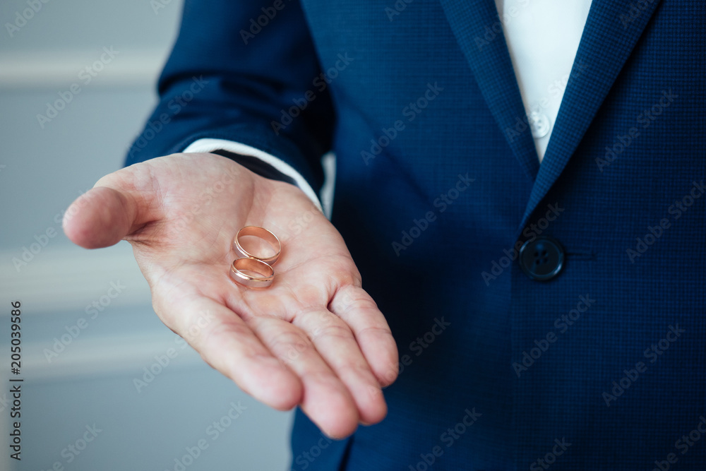 the groom in an elegant suit is holding engagement rings in his hand