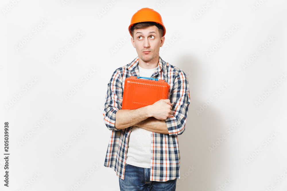 Young curious handsome man in protective orange hardhat holding case with instruments or toolbox isolated on white background. Instruments, tools for renovation apartment room. Repair home concept. Young curious handsome man in protective orange hardhat holding case with instruments or toolbox isolated on white background. Instruments, tools for renovation apartment room. Repair home concept.