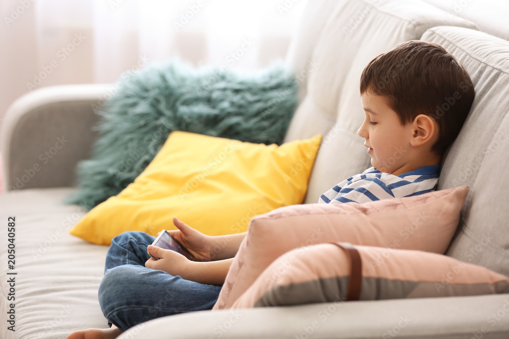 Cute little boy with mobile phone on sofa at home Cute little boy with mobile phone on sofa at home