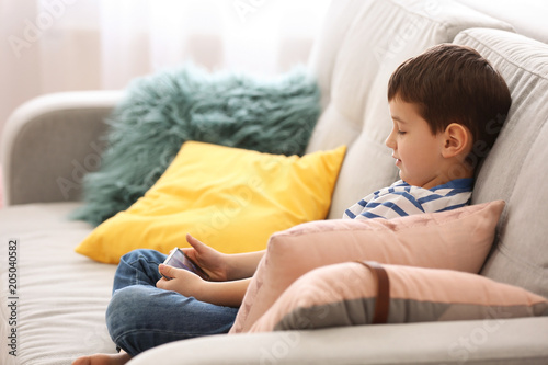 Cute little boy with mobile phone on sofa at home