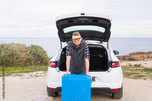 Man standing in back of car smiling and getting ready to go. Young laughing mle standing near open trunk of a car. Summer road trip © satura_