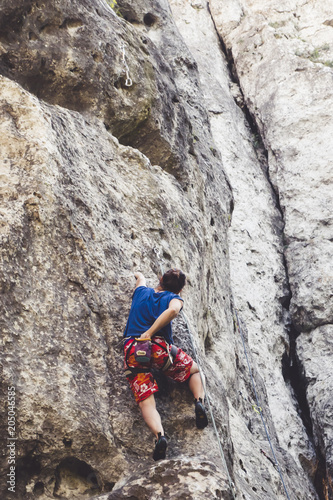 Young girl climber climbs a steep rock