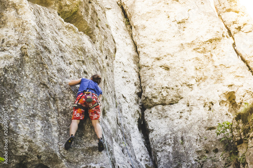 Young girl climber climbs a steep rock at sunset