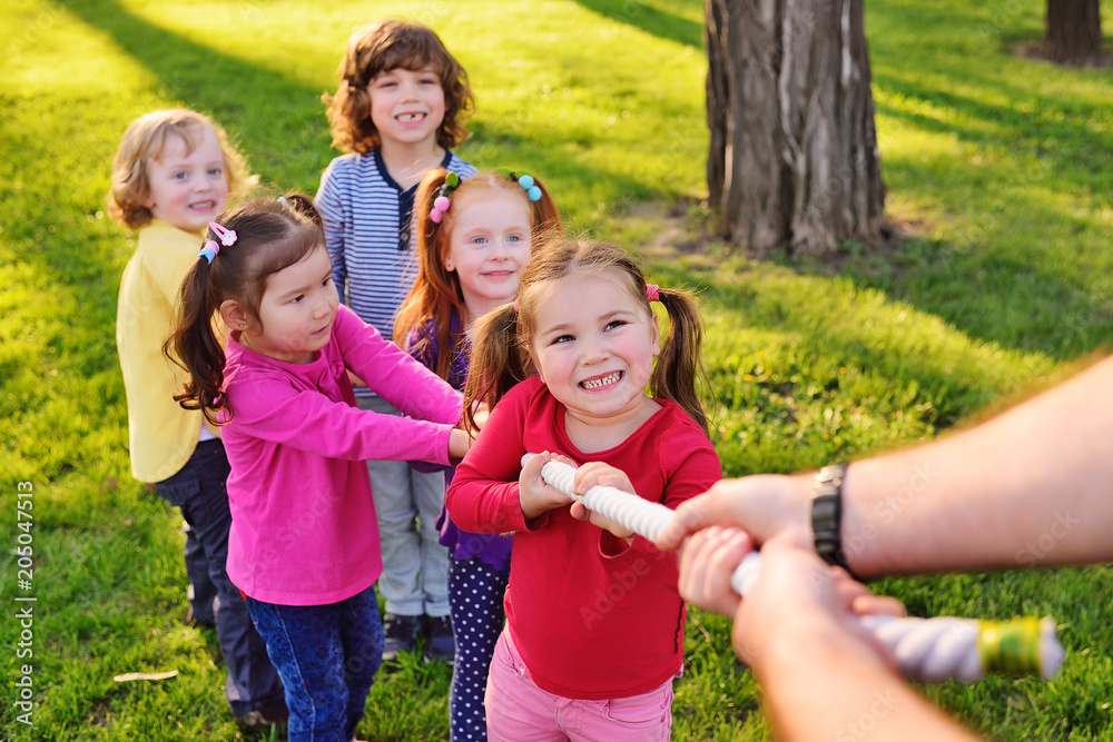 Fototapeta premium a group of small preschool children play a tug of war in the park. Outdoor games, childhood, friendship, leadership, children's day.