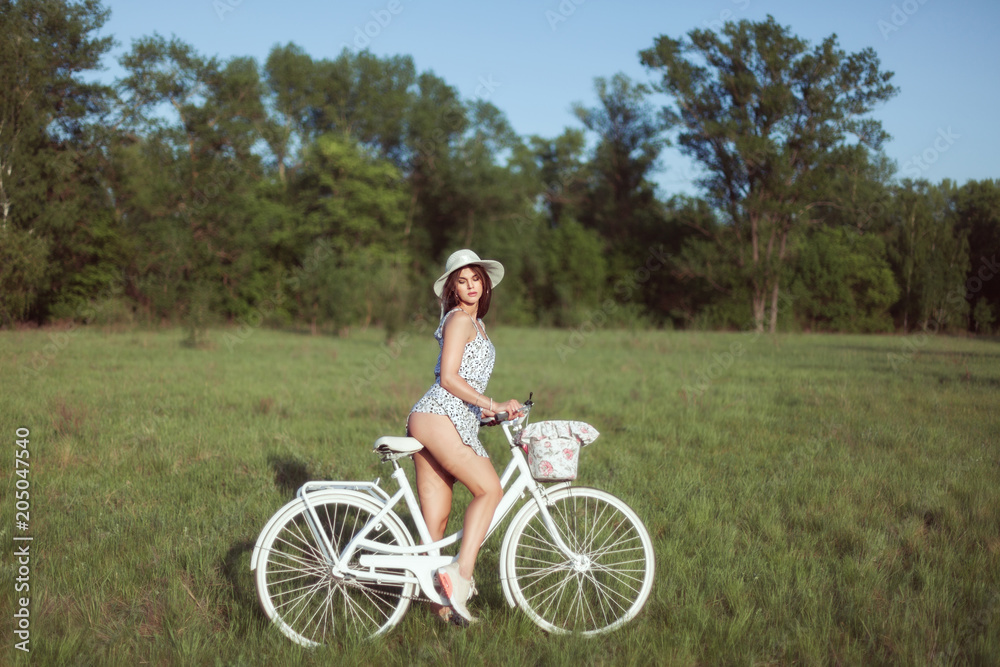 Young woman sits on a white bicycle on a meadow.
