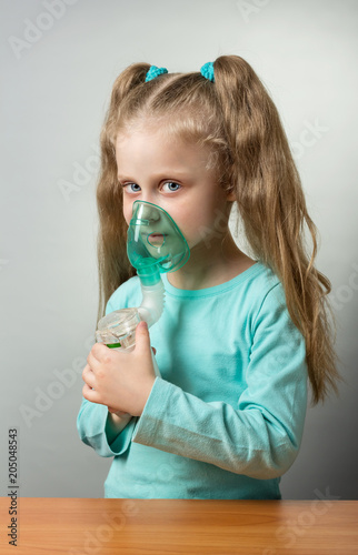 Mesh nebulizer with child mask in hands of sick child, on grey