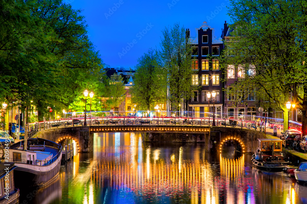 Amsterdam canal with typical dutch houses and bridge during twilight blue hour in Holland, Netherlands.