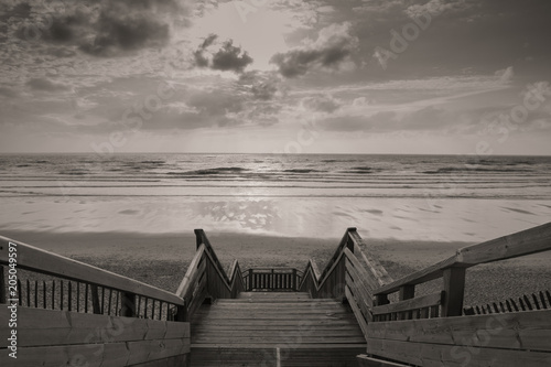 scenic biscarrosse beach in sunset with clouds and wooden footpath stairs in black and white sepia, france photo